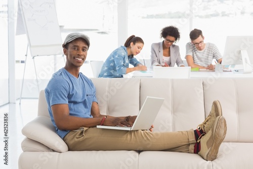 Man using laptop with colleagues in background at creative