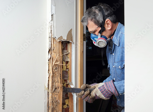 Man removing termite damaged wood from wall