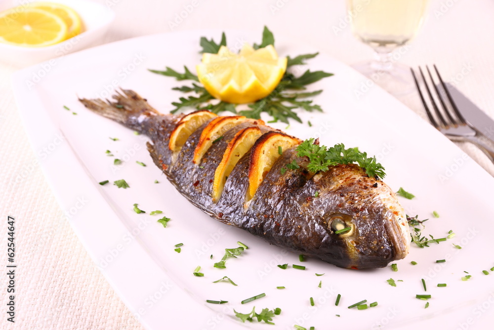 Grilled sea bream fish, lemon, arugula on white plate Grilled sea bream fish, lemon, arugula on white plate