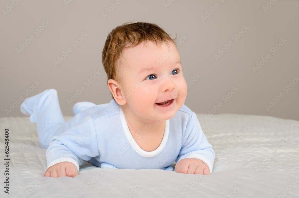 Cute smiling baby boy in bed lying on his belly in bedroom Cute smiling baby boy in bed lying on his belly in bedroom