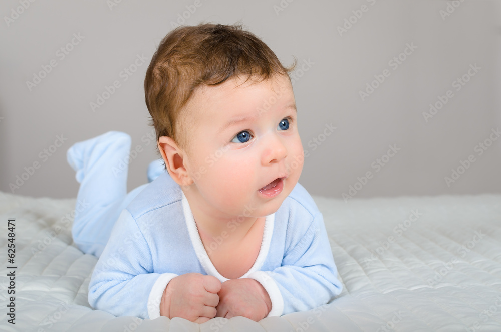 Cute smiling baby boy in bed lying on his belly in bedroom Cute smiling baby boy in bed lying on his belly in bedroom
