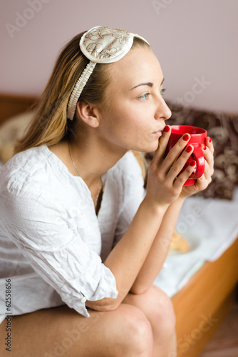 dreamy young woman with a sleepmask & cup of hot drink
