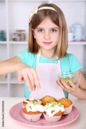 Little girl decorating cupcakes in kitchen at home