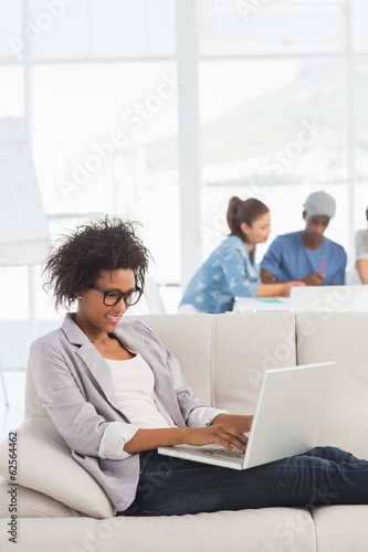 Woman using laptop with colleagues in background at creative
