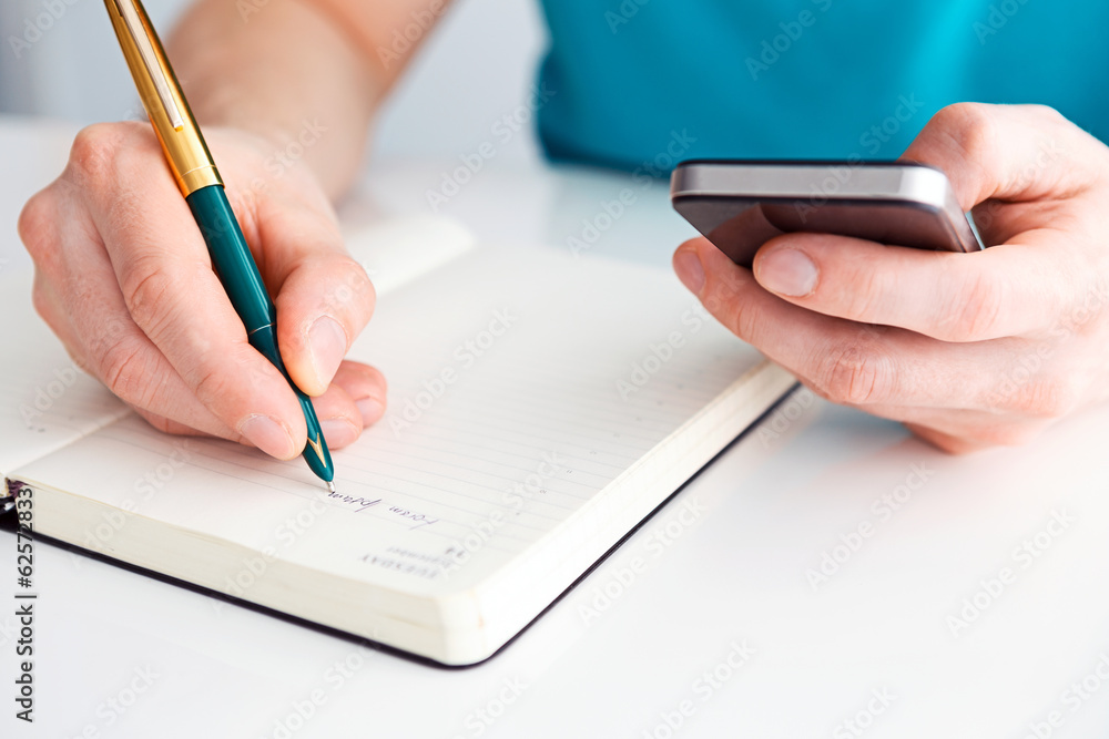 Man's hand writes a pen in your diary and second holding a mobil Man's hand writes a pen in your diary and second holding a mobil