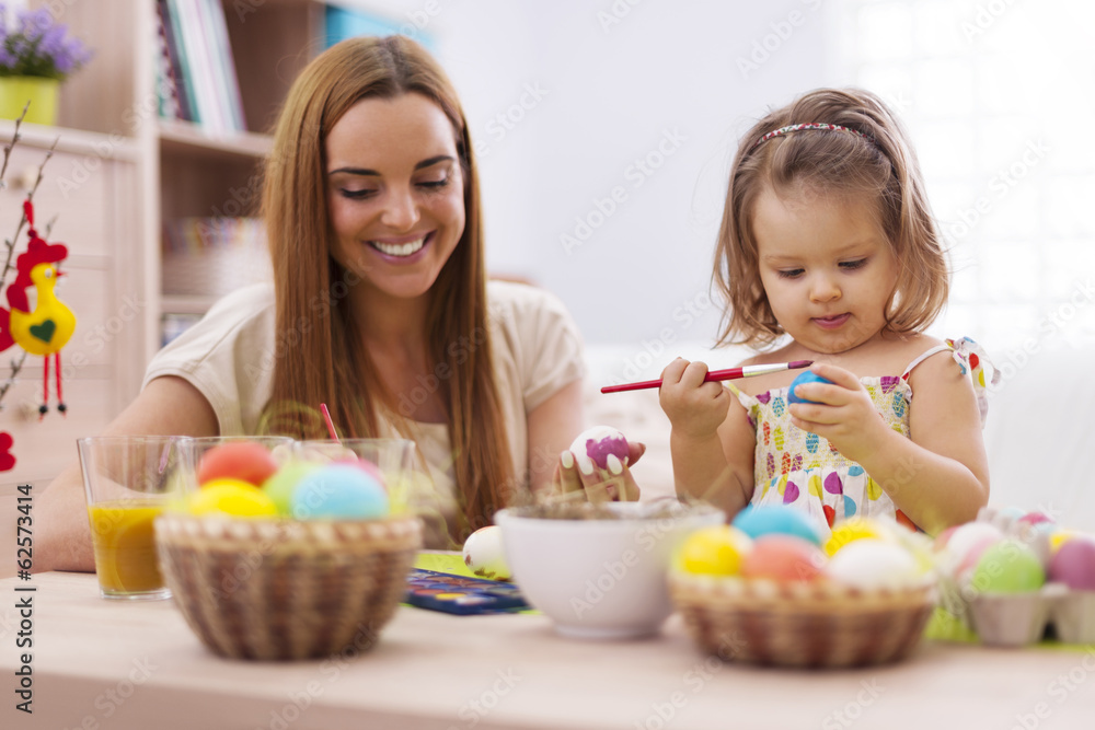 Focus little girl painting easter eggs with her mother