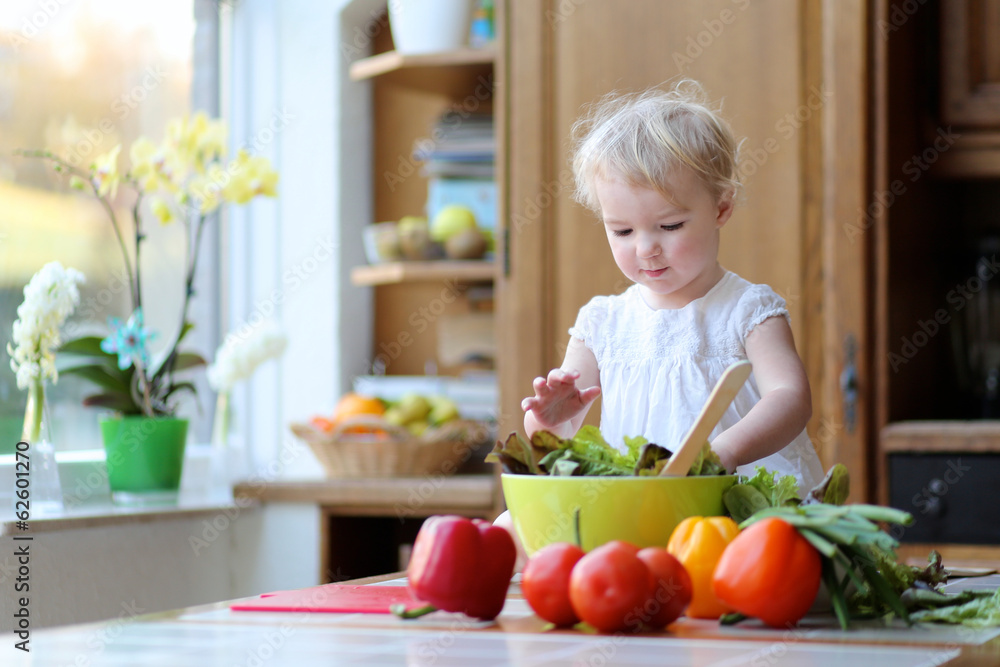 Funny toddler girl mixing vegetables in the bowl preparing salad Funny toddler girl mixing vegetables in the bowl preparing salad