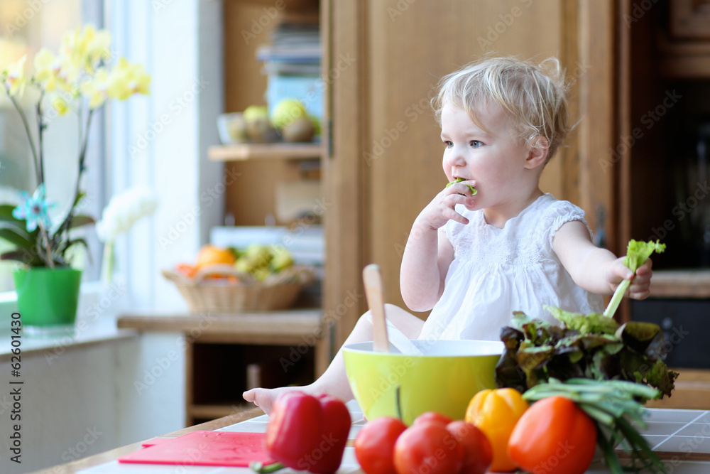 Funny toddler girl mixing vegetables in the bowl preparing salad Funny toddler girl mixing vegetables in the bowl preparing salad