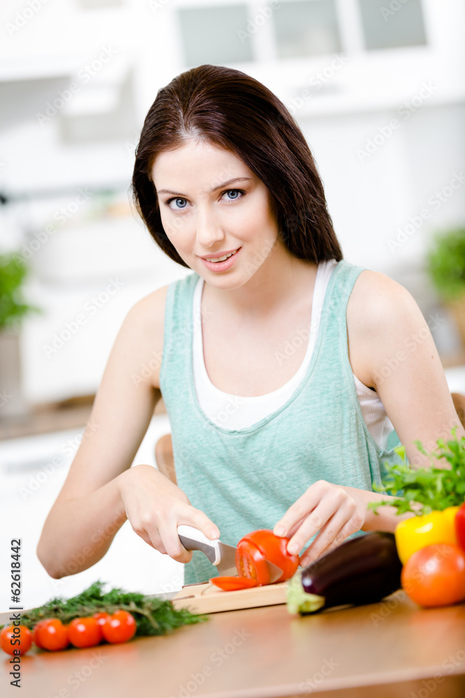 Woman chops groceries for salad sitting at the kitchen table