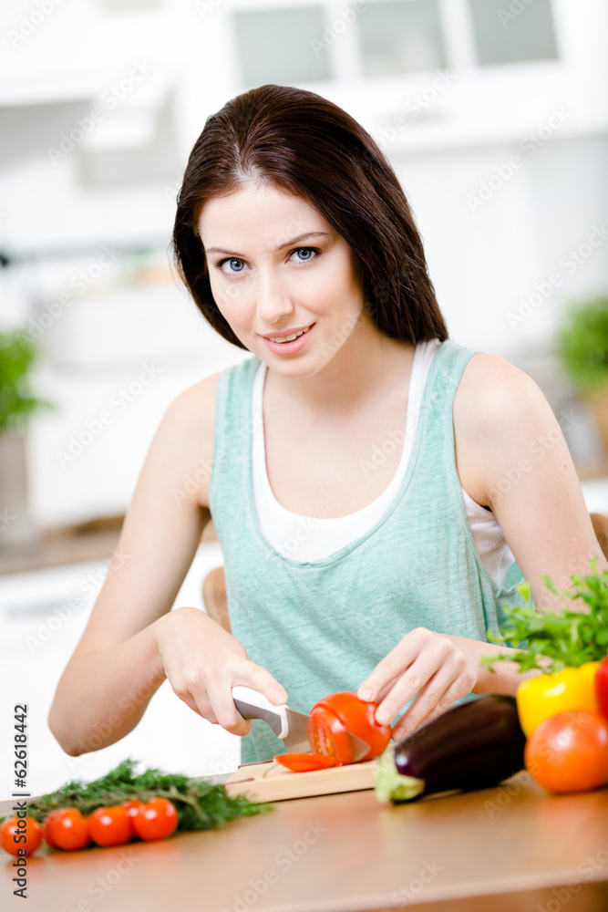 Woman chops groceries for salad sitting at the kitchen table Woman chops groceries for salad sitting at the kitchen table