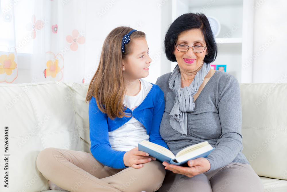 Grandmother and little girl reading a book together at hom Grandmother and little girl reading a book together at hom