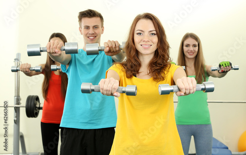 Young beautiful peoples engaged with dumbbells in gym