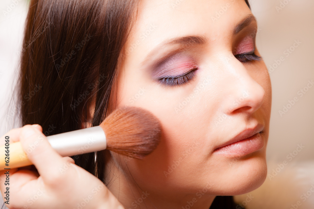 Makeup artist applying with brush powder rouge on female check Makeup artist applying with brush powder rouge on female check