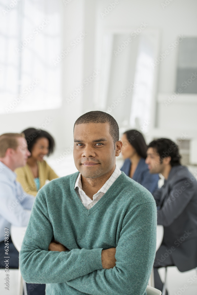Business Meeting. A Group Sitting Down Around A Table. A Man Smiling Confidently. Business Meeting. A Group Sitting Down Around A Table. A Man Smiling Confidently.