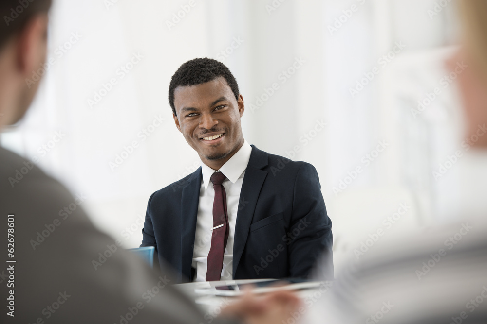 Office Interior. Three People Sitting Around A Table At A Business Meeting. A Man In A Suit With A Cup Of Coffee. A Digital Tablet On The Table. Office Interior. Three People Sitting Around A Table At A Business Meeting. A Man In A Suit With A Cup Of Coffee. A Digital Tablet On The Table.