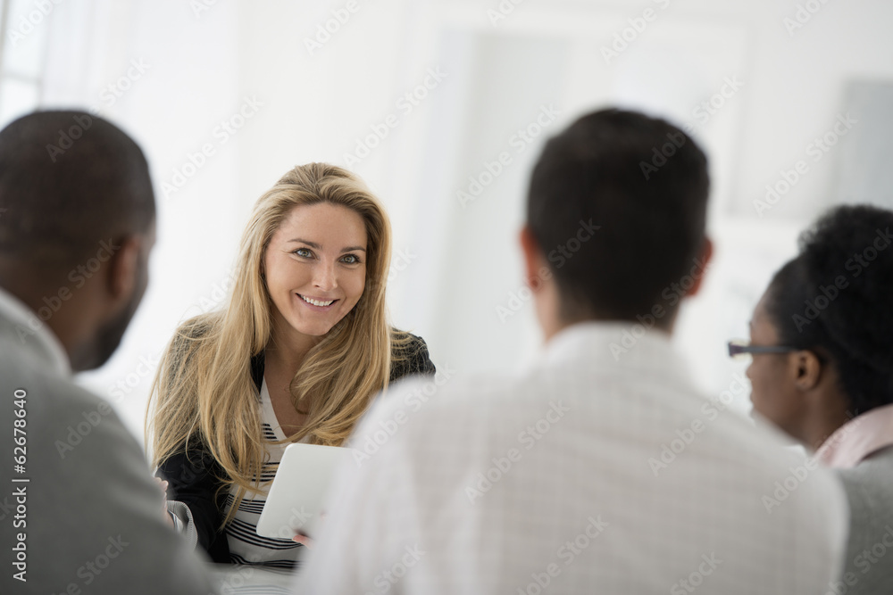Office Interior. A Group Of Four People, Two Men And Two Women, Seated Around A Table. Business Meeting.