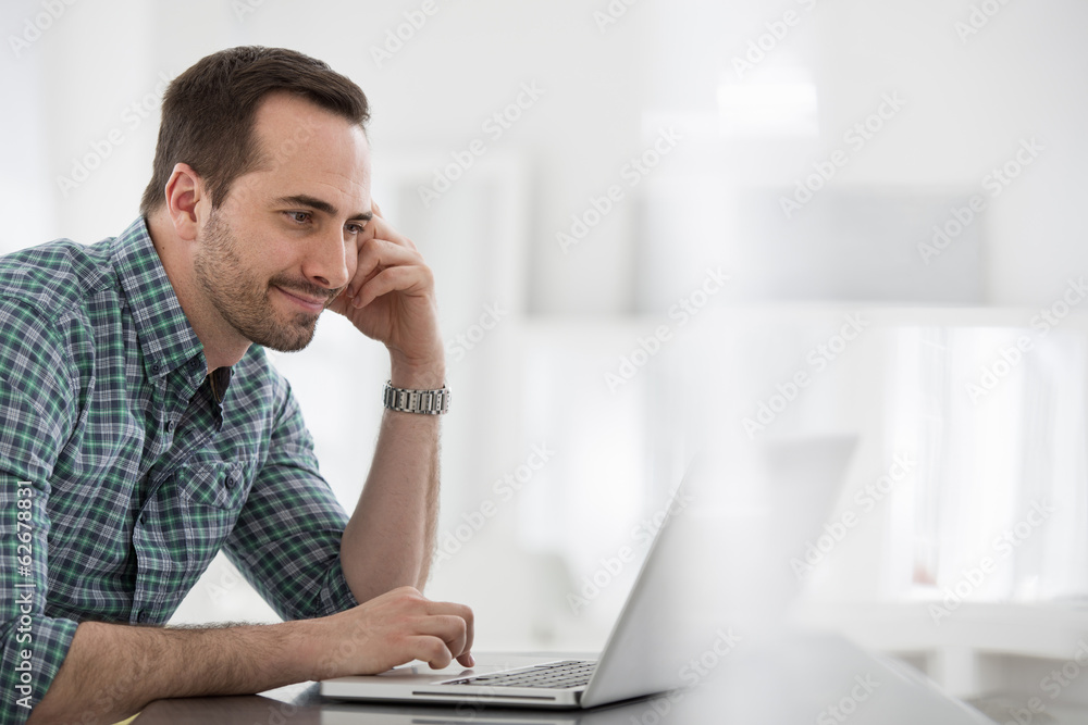 Office Interior. A Man Seated At A Table, Using A Laptop Computer. Office Interior. A Man Seated At A Table, Using A Laptop Computer.