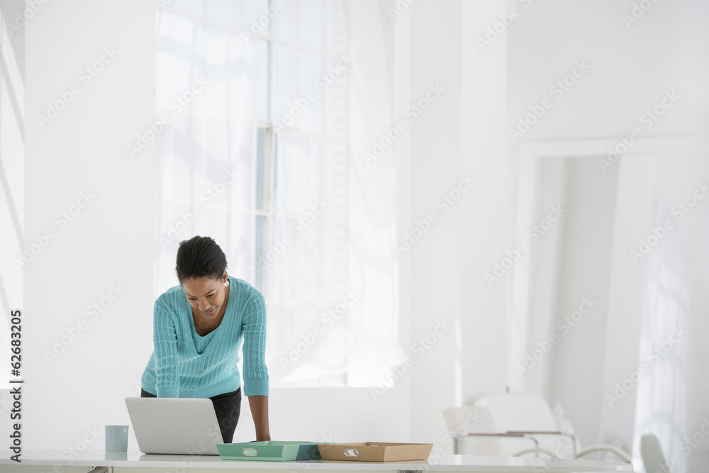 Business. A Woman Leaning Over A Desk Using A Laptop Computer. Business. A Woman Leaning Over A Desk Using A Laptop Computer.