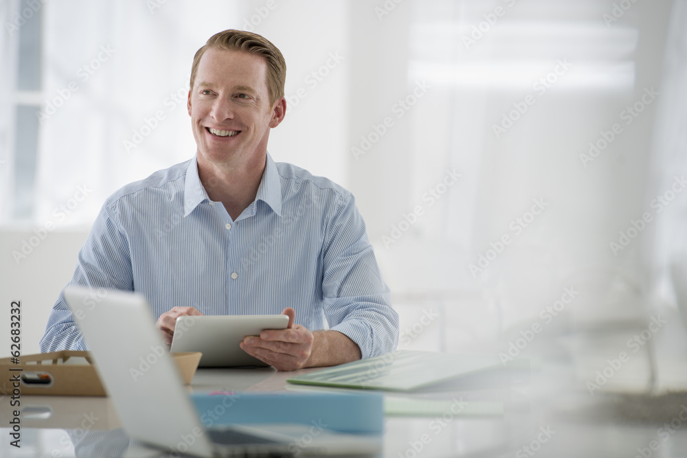 Business. A Light Airy Office Environment. A Man Sitting Holding A Digital Tablet. Business. A Light Airy Office Environment. A Man Sitting Holding A Digital Tablet.