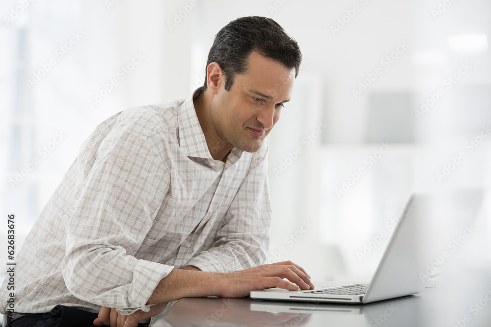 Office Interior. A Man Seated At A Table, Using A Laptop Computer. Office Interior. A Man Seated At A Table, Using A Laptop Computer.