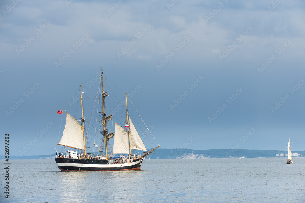 Tall ship on blue water against stormy clouds. Horizontal