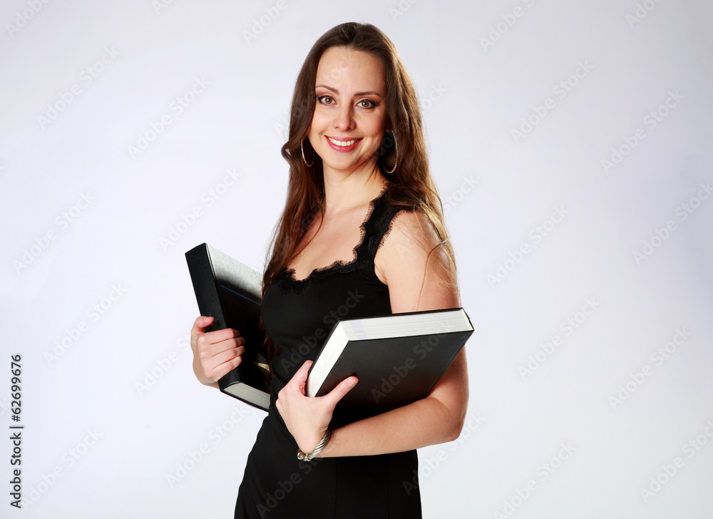 Smiling woman standing and holding books over gray background Smiling woman standing and holding books over gray background
