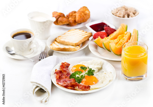 Breakfast with fried eggs, coffee, juice, croissant and fruits