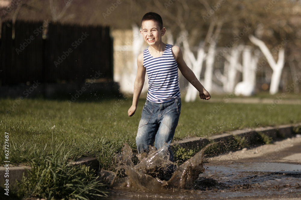 little happy boy jumping in puddle