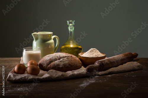 Still life photo of bread and flour with milk and eggs at the wo