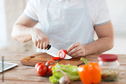 Fototapeta Naklejka Na Ścianę i Meble -  male hand cutting tomato on board with knife