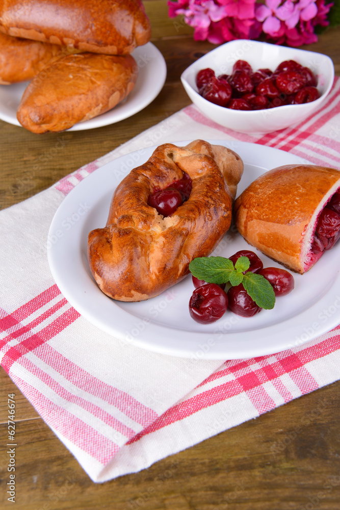Fresh baked pasties with cherry on plate on table close-up Fresh baked pasties with cherry on plate on table close-up