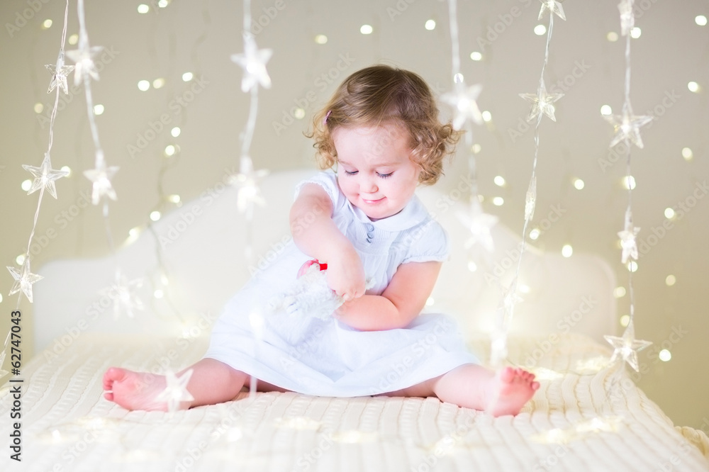 Adorable toddler girl playing with a toy on a white bedroom