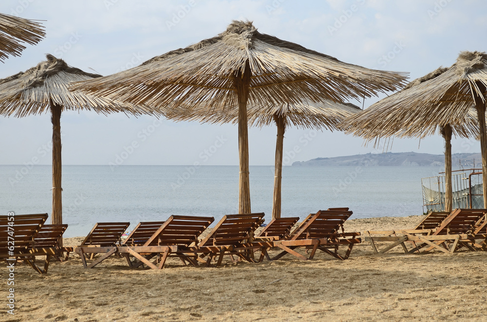 Wooden chaise lounges and beach umbrellas from a reed on a deser