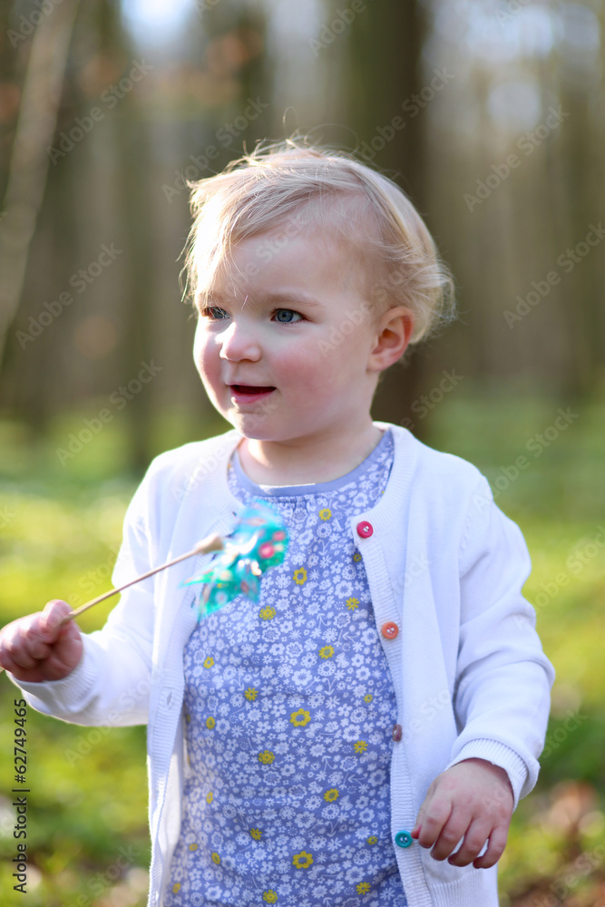 Cute toddler girl playing in spring forest holding pinwheel toy Cute toddler girl playing in spring forest holding pinwheel toy