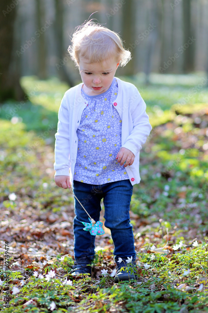 Cute toddler girl playing in spring forest holding pinwheel toy Cute toddler girl playing in spring forest holding pinwheel toy
