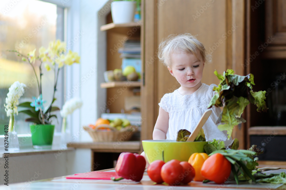 Funny toddler girl mixing vegetables in the bowl preparing salad Funny toddler girl mixing vegetables in the bowl preparing salad