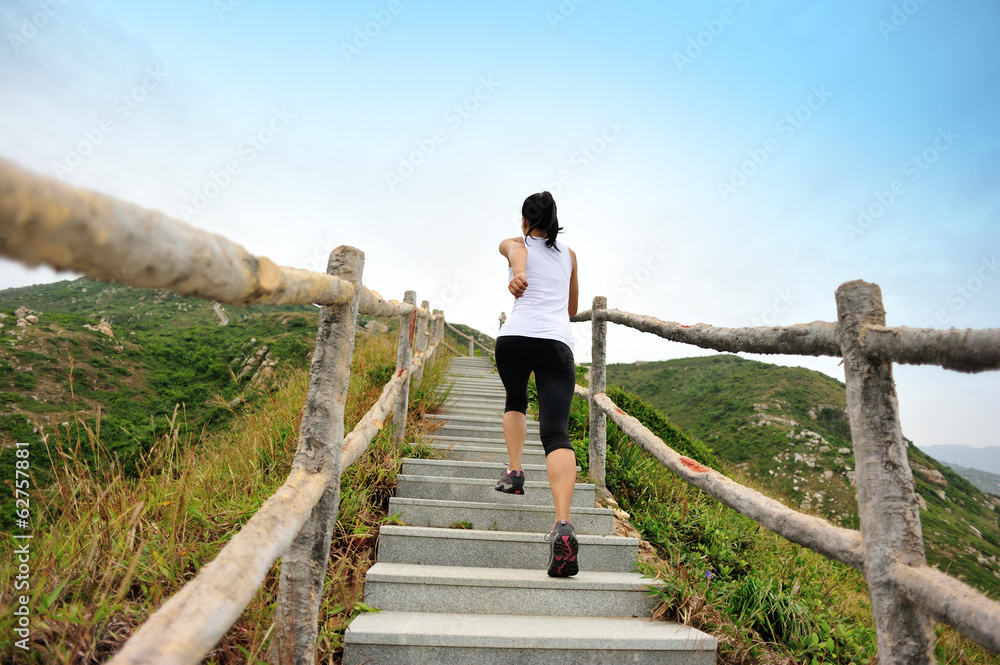 fitness woman running up at stone stairs to mountain peak