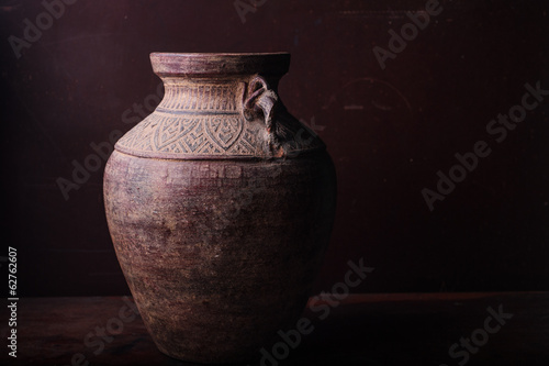 Earthenware jug standing on dark room or tiles  with copyspace