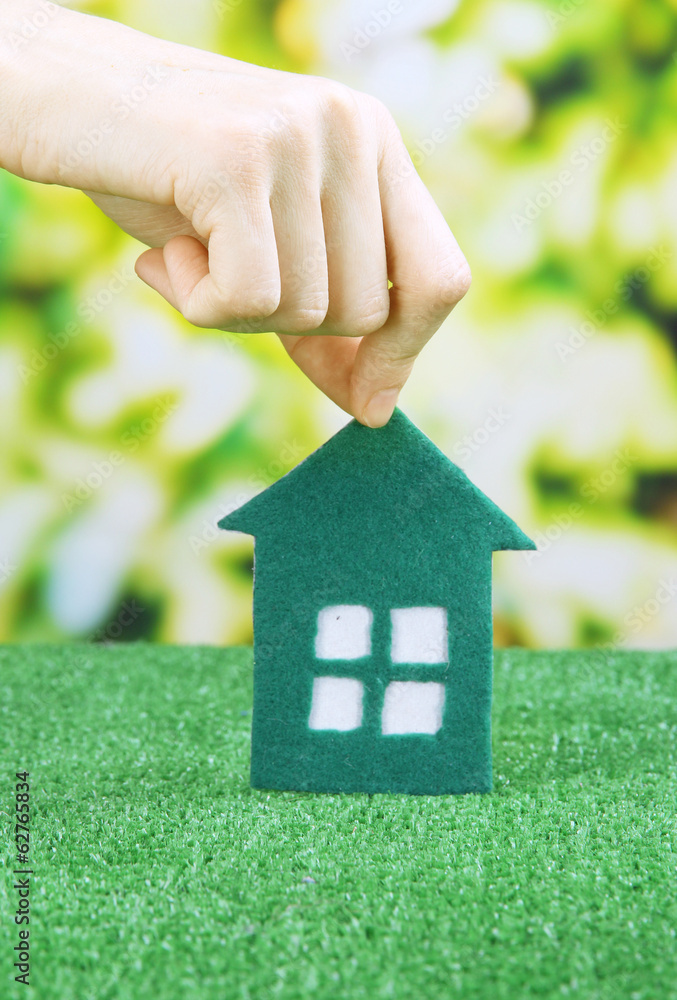 Little paper house in hand on green grass on bright background Little paper house in hand on green grass on bright background
