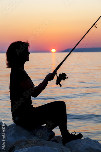 Woman silhouette fishing on rock