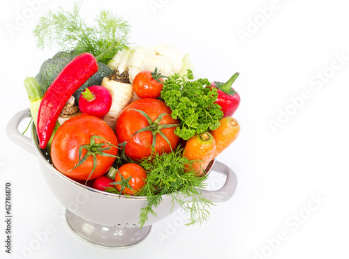 Fresh vegetables in metal colander over white