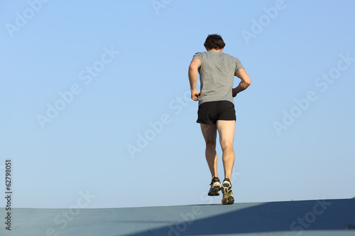 Back view of a jogger man running against blue sky