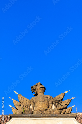 Stone knight armor statue on a roof under blue sky