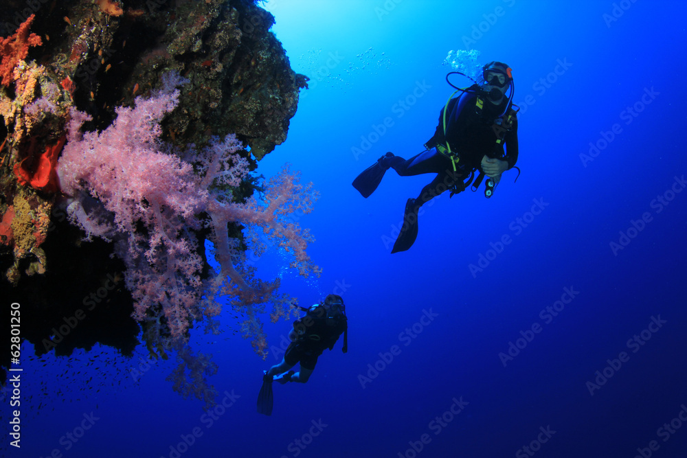 Scuba divers explore coral reef wall
