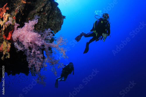 Scuba divers explore coral reef wall