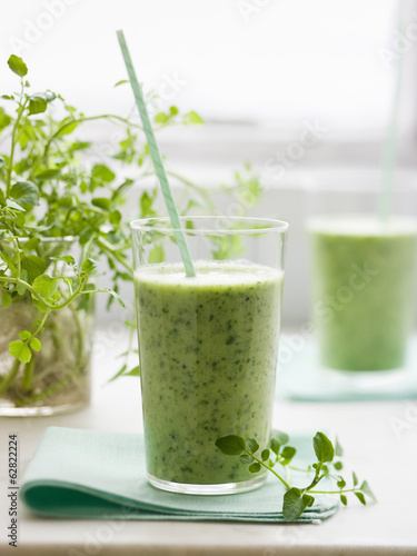 Two glasses of a healthy green smoothie herb drink with a straw. 