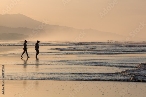 Silhouette of two people walking on the beach with beutuful ligh
