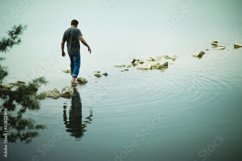 Man walking barefoot on stepping stones in lake photo