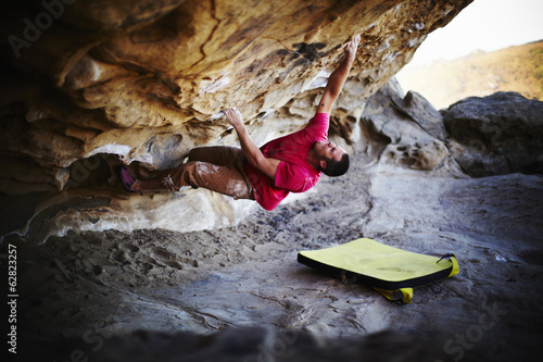A man free climbing on the overhang of a rock face, with minimum equipment. 