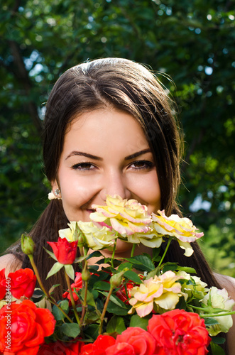 Beautiful woman in the flower garden smelling red yellow roses.